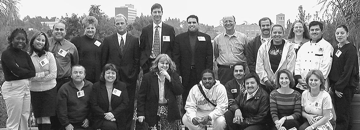 Black and white photo of a group of mentorship members posing fort the camera with the view of the UCLA campus in the background. Photo appears like it is from 2003.